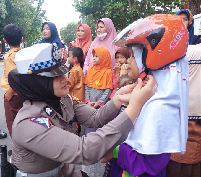 Sumber/foto : ntmcpolri/ Polwan satlantas Polresta Pekanbaru Memasang Helm kepada Anak Sekolah.(doc) 