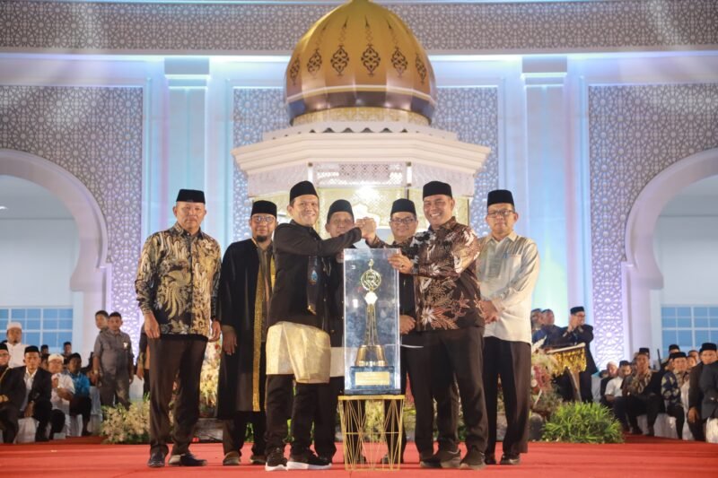 Bupati Aceh Besar H Muharram Idris (Syech Muharram) menerima piala bergilir juara umum MTQ ke-37 Aceh tahun 2025, dari Wakil Gubernur Aceh Fadhlullah SE, pada malam penutupan, di Arena Utama, Komplek Perkantoran Pemkab Pidie Jaya, Jumat (7/11/2025) malam. FOTO/ PROKOPIM PEMKAB ACEH BESAR